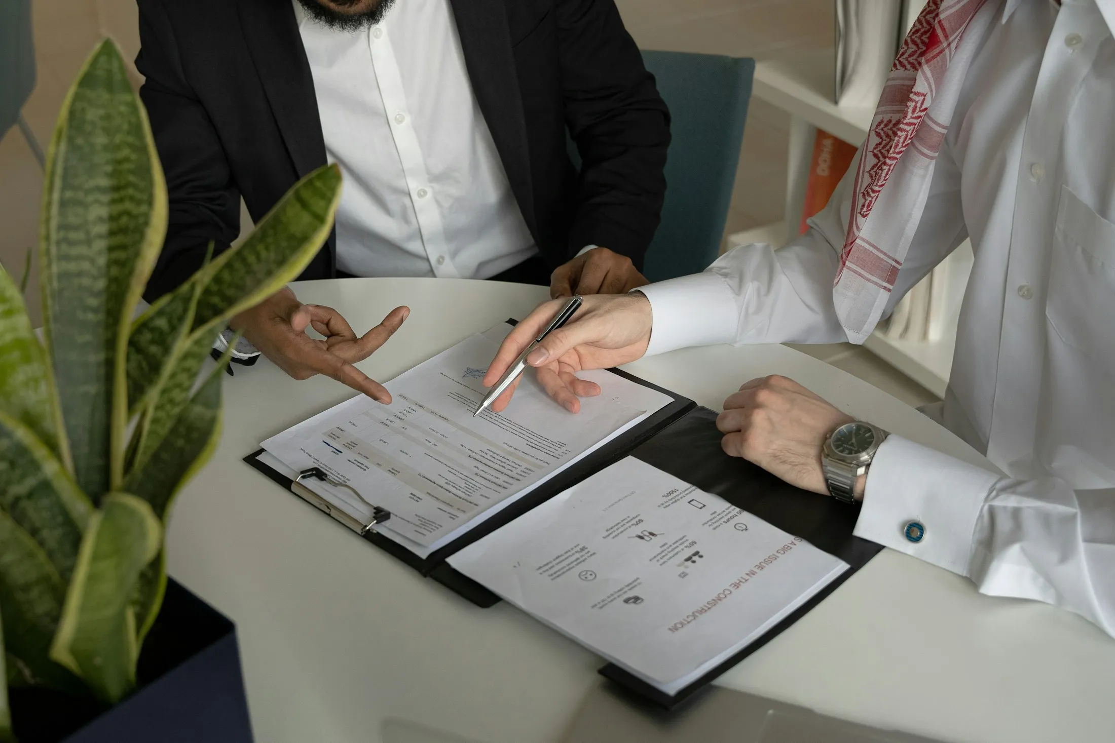 A client in a kandura reviews documents with an advisor at a white desk